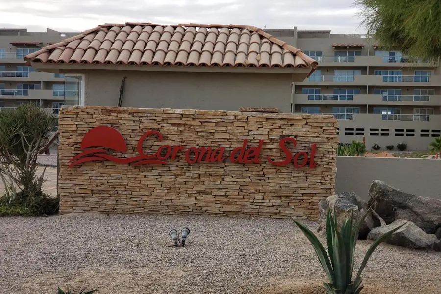 Stone “Corona del Sol” sign at the condominium entrance, with agaves and the buildings behind, in Las Conchas, Puerto Peñasco